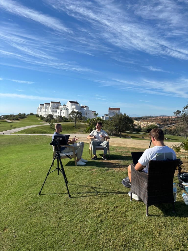 Opname op een golfbaan aan de Costa del Sol: camera op statief, twee mensen in gesprek en een operator die meekijkt
